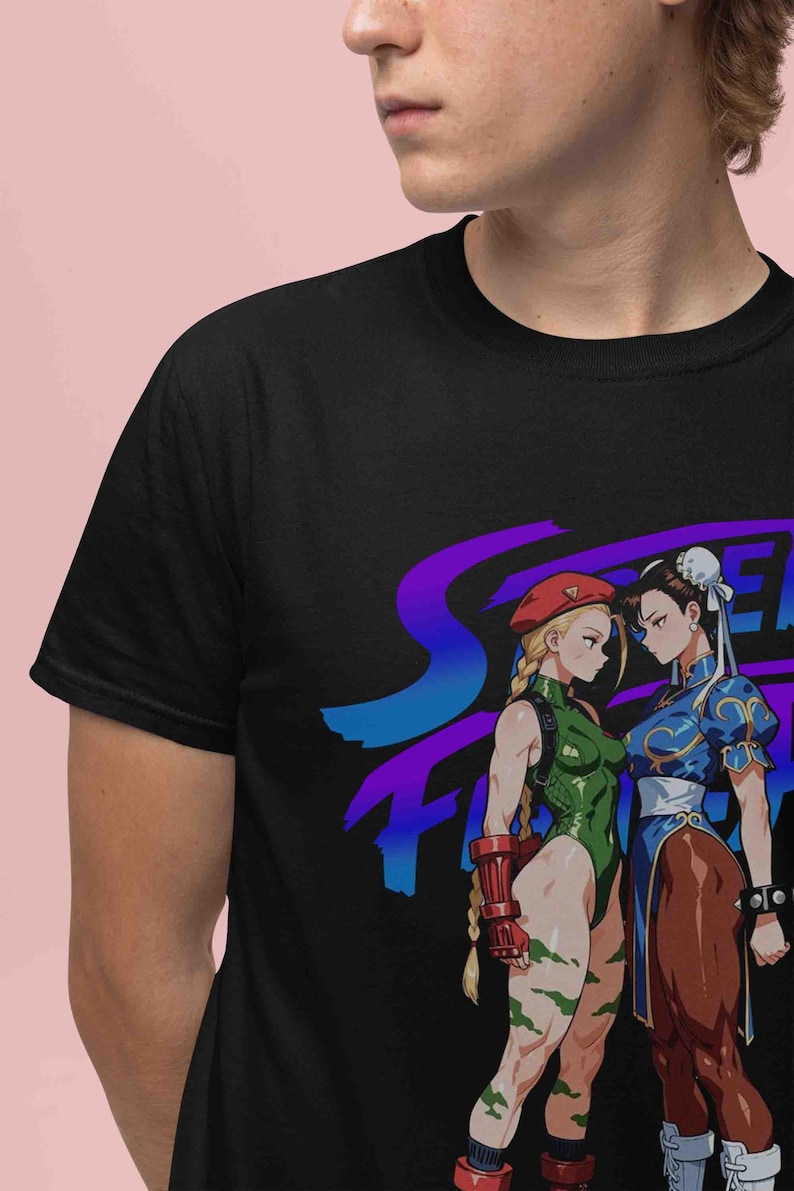 May include: Black t-shirt featuring a graphic of two female characters from the Street Fighter video game. One character wears a green bodysuit and the other a blue dress. The shirt has the Street Fighter logo in blue and purple.