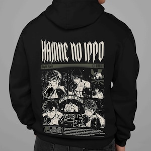 May include: Black hoodie featuring a graphic design from the anime series "Hajime no Ippo." The design includes the series title, illustrations of boxing characters, and Japanese text. The hoodie has a hood and a kangaroo pocket.