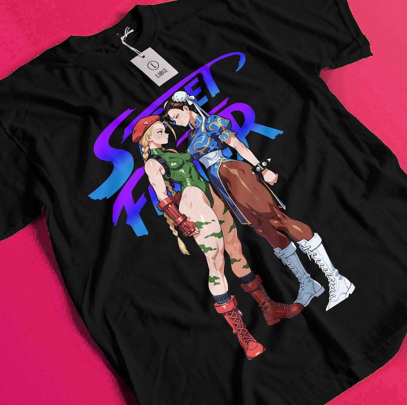 May include: Black t-shirt featuring a graphic of two female characters from the Street Fighter video game series. The design includes the word "Street Fighter" in a purple and blue gradient. The characters are in fighting poses.