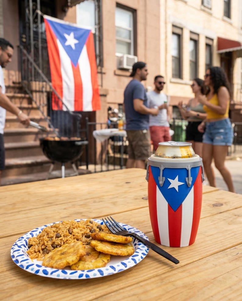May include: A cylindrical beverage cooler designed to resemble a conga drum, featuring the red, white, and blue colours of the Puerto Rican flag with a white star. A plate of rice with beans and fried plantains sits next to a black plastic fork.