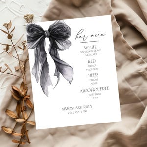 May include: A white bar menu card with a large, elegant black bow illustration. The menu lists options for white and red wine, beer, and alcohol-free beverages. The names "Simone and Riley" and a date are printed at the bottom.