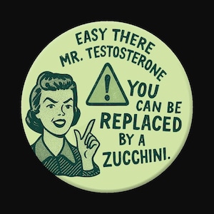May include: A round, light green button with a retro illustration of a woman pointing. Text reads "EASY THERE MR. TESTOSTERONE YOU CAN BE REPLACED BY A ZUCCHINI" with a warning symbol.