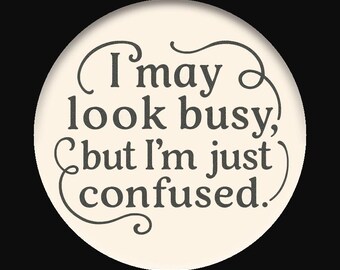 May include: A round, off-white button with the text "I may look busy, but I'm just confused" in dark gray script. The text is surrounded by decorative swirls, set against a black background.