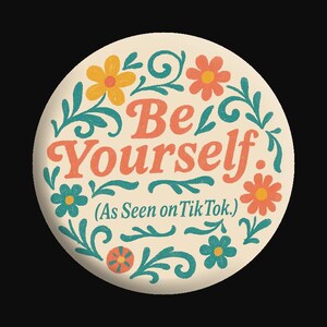May include: Round button with the words "Be Yourself" in orange script, surrounded by teal and orange floral designs. The text "(As Seen on TikTok.)" is below the main text, all on a cream background.