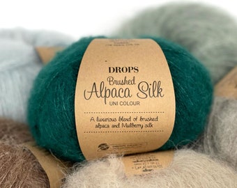 May include: Close-up of four skeins of yarn in different colours: light blue, teal, brown, and beige. The teal skein has a label that reads "DROPS Brushed Alpaca Silk UNI COLOUR A luxurious blend of brushed alpaca and Mulberry silk."