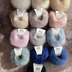 May include: Twelve balls of yarn in a variety of colours, including white, beige, pink, grey, blue and black. Each ball has a label with a number and the text "FARBE-COL. PARTIE-LOT".