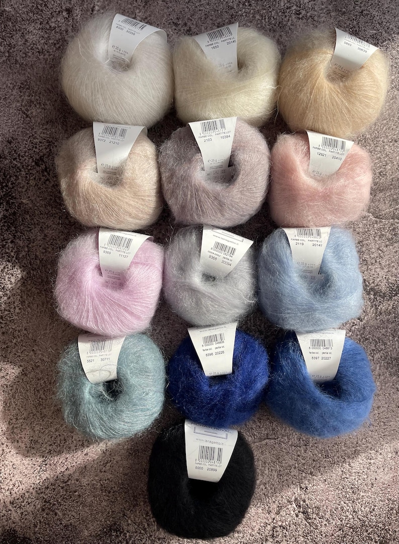 May include: Twelve balls of yarn in a variety of colours, including white, beige, pink, grey, blue and black. Each ball has a label with a number and the text "FARBE-COL. PARTIE-LOT".