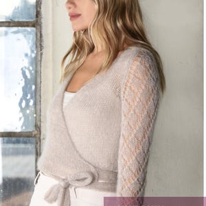 May include: A light beige wrap cardigan with a delicate openwork pattern on the sleeves. The cardigan is tied at the waist with a long sash.