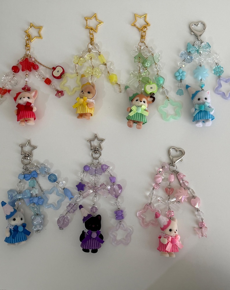 May include: Seven decorative keychains featuring small animal figurines wearing party hats and dresses. Each keychain includes colorful beads, star-shaped charms, and metal clasps in red, yellow, green, blue, purple, and pink color themes.