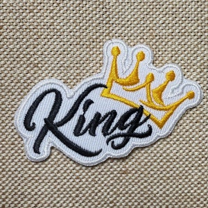 Puede incluir: Parche blanco bordado con la palabra "King" en letras cursivas negras y una corona dorada encima.