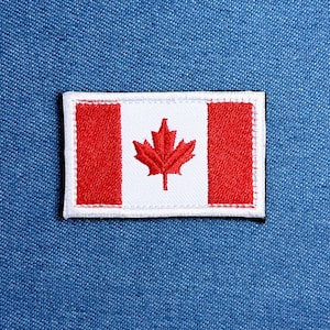 May include: Embroidered patch featuring the Canadian flag. The flag design includes a white background with a red maple leaf in the center, flanked by two red vertical bars. The patch has a white border and is set against a blue denim background.