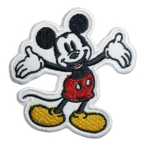 Può includere: Una toppa ricamata bianca con Mickey Mouse con le braccia aperte, che indossa i suoi pantaloncini rossi e le scarpe gialle.