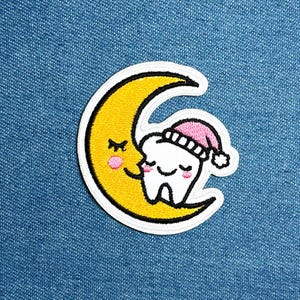 May include: Embroidered patch showing a yellow crescent moon with a smiling face and a white tooth wearing a pink nightcap. The tooth is nestled in the moon's embrace, with closed eyes and rosy cheeks. The patch has a white border.