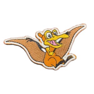 Puede incluir: Un parche bordado de un pterodáctilo de dibujos animados con plumas naranja y marrón, un pico amarillo y un contorno blanco. El pterodáctilo está volando con las alas extendidas.