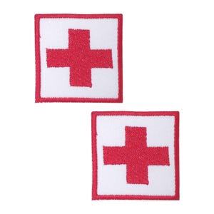 Könnte beinhalten: Zwei rote gestickte medizinische Kreuz-Patches auf weißem Hintergrund. Die Patches sind quadratisch mit einem roten Rand.