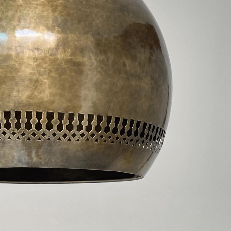 Op de afbeelding: Een ronde, messing hanglamp met een decoratief, uitgesneden ontwerp rond de onderkant.