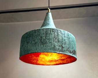 May include: A hanging pendant light fixture with a weathered, turquoise-green exterior and a bright orange-red interior. The light has a cylindrical shade with a conical top and is suspended by a black cord.