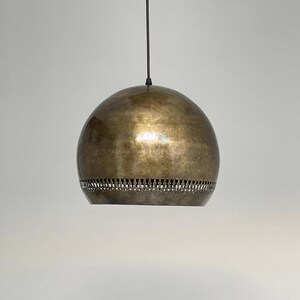 Op de afbeelding: Een hanglamp in goudkleur met een ronde, gehamerde metalen kap. De kap heeft een decoratieve band met gaten rond de onderkant.
