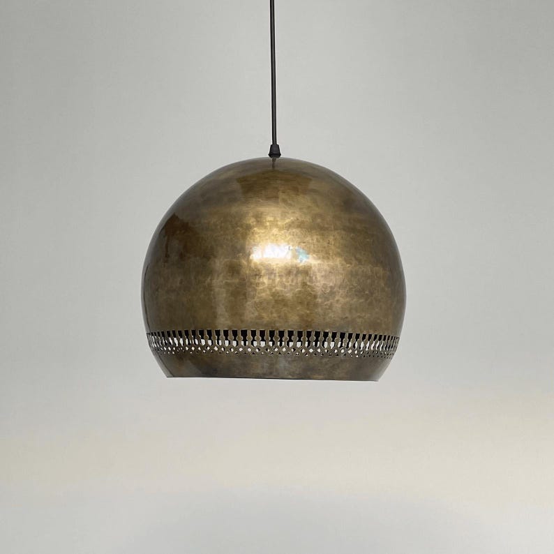 Op de afbeelding: Een hanglamp in goudkleur met een ronde, gehamerde metalen kap. De kap heeft een decoratieve band met gaten rond de onderkant.