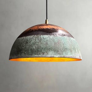 May include: A dome-shaped pendant light with a textured, multi-toned finish. The top section is a rusty orange, transitioning to a dark brown band, then a green-blue patina. The interior glows with a warm, golden light.