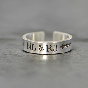May include: A silver ring inscribed with "NL & RJ" and a row of small stars on the band.