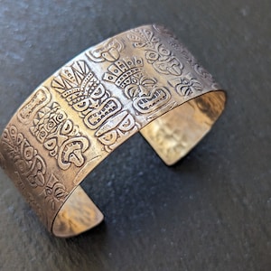 May include: A silver bracelet with a textured design of tiki faces and other patterns.