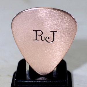 May include: A rose gold guitar pick with the initials "R.J." engraved on the front.