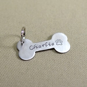 May include: Silver bone-shaped dog tag with a paw print and the name "Charlie" engraved on it.