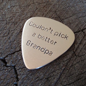 May include: Silver guitar pick with the text "Couldn't pick a better Grandpa" engraved on it.