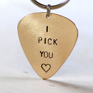 May include: Gold guitar pick keychain with the words "I pick you" and a heart engraved on it.
