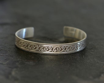 May include: A silver bangle bracelet with an intricate floral design.