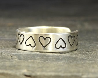 May include: A silver ring with a band of hearts etched into the metal.