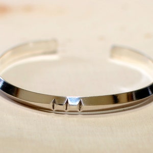 May include: A silver bangle bracelet with a textured, slightly raised design on the front.