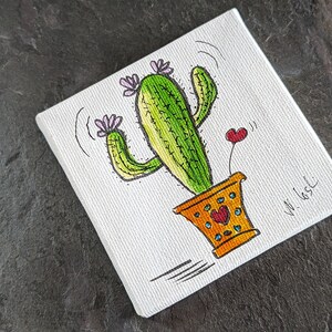 Puede incluir: Un lienzo pintado a mano con un cactus de dibujos animados con flores rosas y un coraz&oacute;n. El cactus est&aacute; en una maceta amarilla con detalles naranja y marr&oacute;n. El lienzo est&aacute; firmado "W. 165C".