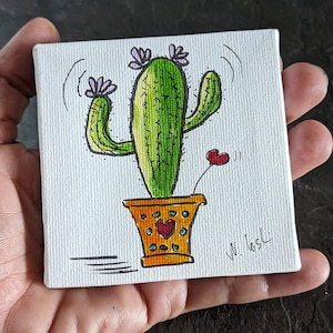 Puede incluir: Un lienzo pintado a mano con un cactus de dibujos animados con brazos verdes y una maceta amarilla con detalles azules y rojos. El cactus tiene flores rosas y un coraz&oacute;n rojo en un tallo. El lienzo est&aacute; firmado "V.L. Gask".