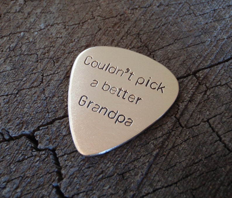 May include: Silver guitar pick with the text "Couldn't pick a better Grandpa" engraved on it.