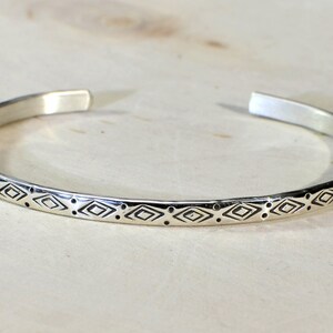 May include: A silver bangle bracelet with a geometric pattern of diamonds and dots.