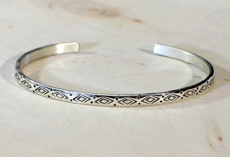 May include: A silver bangle bracelet with a geometric pattern of diamonds and dots.