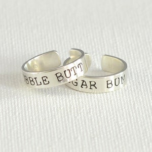 May include: Two silver toe rings with the words "Bubble Butt" and "Sugar Bum" engraved on them.