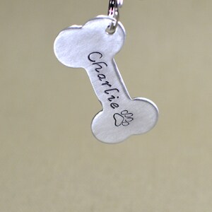 May include: Silver bone-shaped dog tag with the name "Charlie" engraved on it and a paw print below the name.