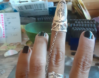 May include: A silver ring with a detailed design featuring a spider and stars. The ring is connected to a chain that hangs down to the wearer's other finger.
