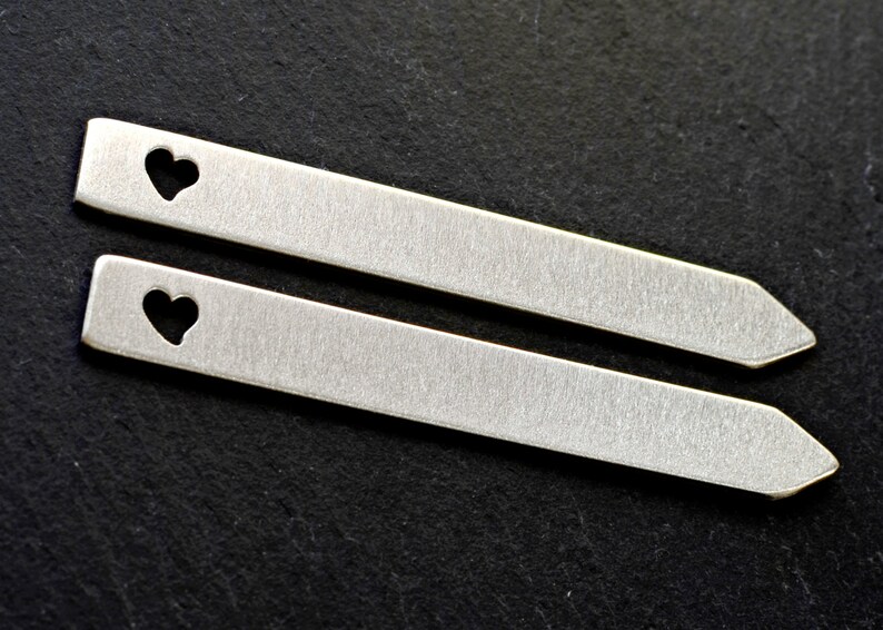 Puede incluir: Dos pasadores de corbata plateados con un dise&ntilde;o de coraz&oacute;n recortado. Los pasadores son lisos y tienen un acabado cepillado.
