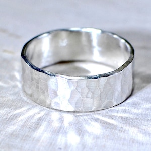 May include: A silver hammered band ring. The ring is wide and has a textured surface.