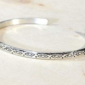 A silver bangle bracelet with a geometric pattern etched into the surface.