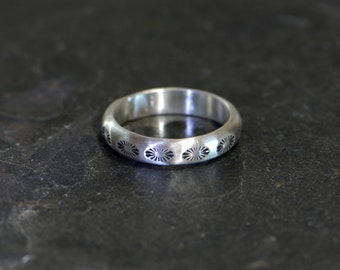 May include: A silver ring with a decorative pattern of small circles around the band.