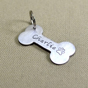 May include: Silver bone-shaped dog tag with the name "Charlie" engraved on it and a paw print design.
