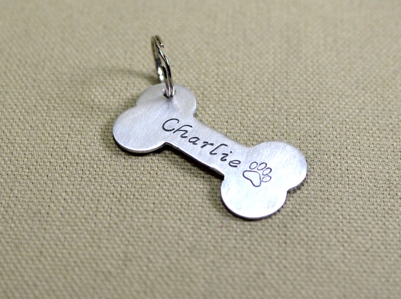 May include: Silver bone-shaped dog tag with the name "Charlie" engraved on it and a paw print design.