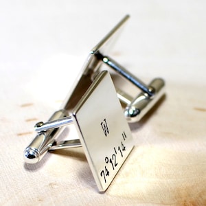 May include: Silver cufflinks with a square design. The cufflinks are engraved with the text "W 74°12'14" "