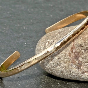 May include: A gold hammered bangle bracelet. The bracelet is made of a single piece of metal and has a smooth, rounded finish.