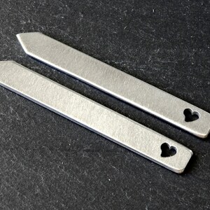 May include: Two silver tie bars with a heart cut-out design.